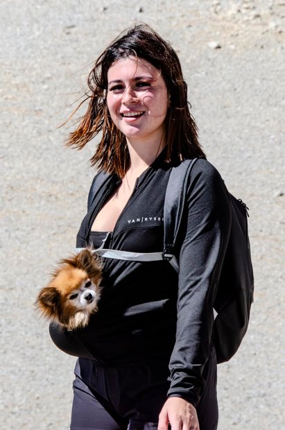 Portrait vertical d’une femme et de son chien dans un sac ventral.